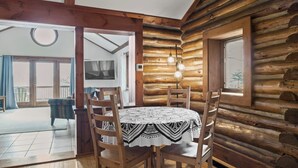 A log cabin interior with a dining table, chairs, and a large window.