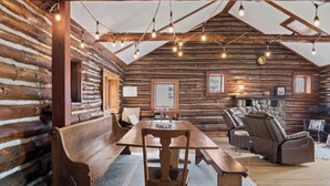 A log cabin interior with a long dining table, benches, a fireplace, and a stone fireplace surround.