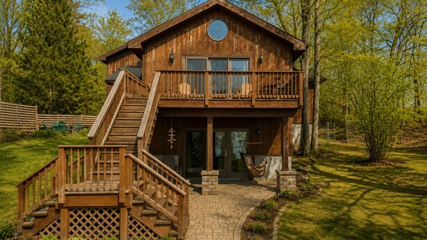 A wooden cabin with a balcony, a staircase, and a brick pathway leading to the entrance.