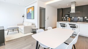 Een moderne woonkamer met een witte bank, een ronde salontafel en een eethoek met een witte tafel en stoelen.