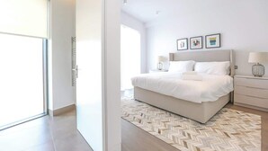 Een moderne slaapkamer met een groot bed, een nachtkastje met een lamp en uitzicht op een balkon.