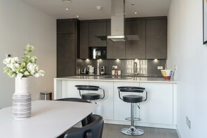 Una cocina moderna con armarios oscuros, una campana extractora de acero inoxidable y una isla blanca con taburetes de bar.