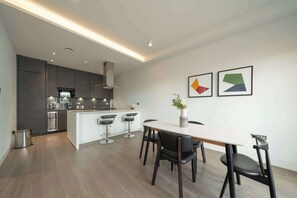 A modern kitchen with a central island, bar stools, and a dining table with chairs. - Beautiful, modern, light flat in Shoreditch (a) (Greater London)