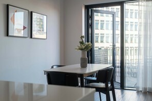 A modern dining area with a table and chairs, a vase with flowers, and a view of buildings through a glass door. - Beautiful, modern, light flat in Shoreditch (a) (Greater London)