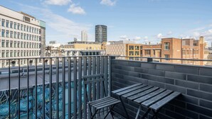 Eine Dachterrasse mit Blick auf die Stadtlandschaft, darunter moderne Gebäude und eine markante, zylindrische Struktur.