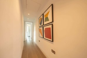 A hallway with a wooden floor and white walls, featuring three framed artworks. - Beautiful, modern, light flat in Shoreditch (a) (Greater London)