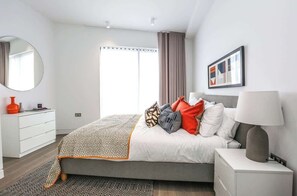 A modern bedroom with a bed, bedside table, lamp, and a large window with curtains. - Beautiful, modern, light flat in Shoreditch (a) (Greater London)