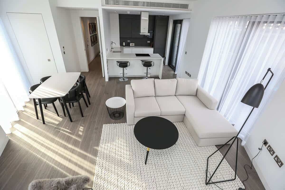 Un salon moderne avec un canapé, une table basse ronde, une table à manger avec des chaises, et un coin cuisine à l’arrière-plan.