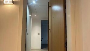 A narrow hallway with a wooden door at the end, a light switch on the wall, and a small step leading to a higher floor.
