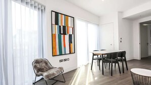 A modern living room with a dining area, a fluffy chair, a large abstract painting, and a view through the window.