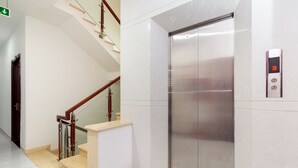 Un ascenseur moderne doté d’un écran numérique, un escalier avec des rampes en verre et un intérieur propre et blanc.