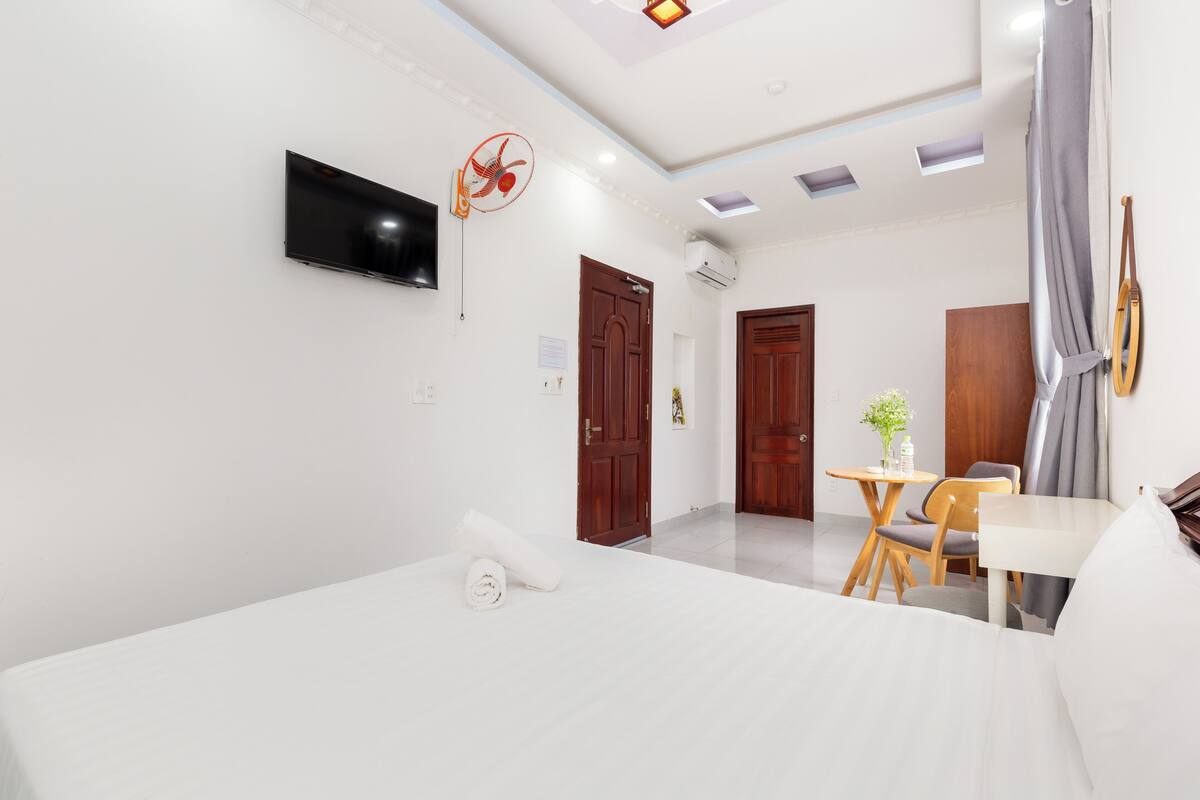 A modern hotel room with a large bed, a flat-screen TV, a ceiling fan, a small table with chairs, and a piano.