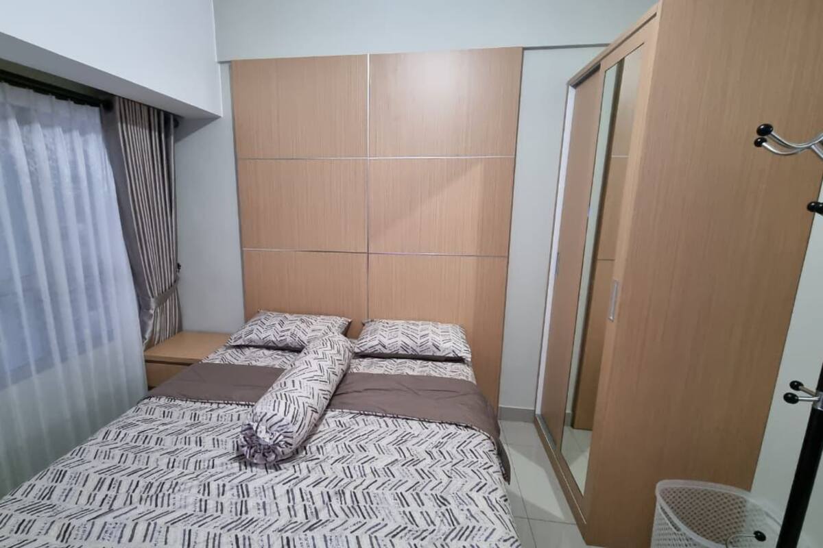 Un dormitorio con cama, armario, espejo y ventana con cortinas.