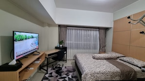 A hotel room with a bed, a desk with a computer, a television, and a window with curtains. - Capital O 93935 Kukami Rooms (Bekasi)