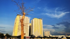 A tall building with multiple floors, surrounded by other buildings and a clear sky. - Capital O 93935 Kukami Rooms (Bekasi)