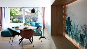 A modern living room with a round dining table, blue sofa, and a large painting on the wall. - Chic and Cosy in Alsace (Hindisheim)