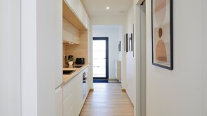 A narrow hallway with wooden flooring, white walls, and a kitchen area on the left. - Chic and Cosy in Alsace (Hindisheim)