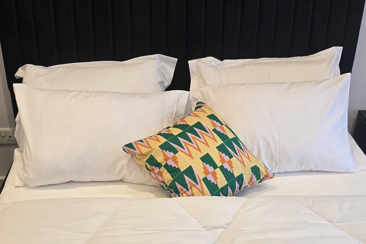 A bed with white bedding and a colorful geometric pillow, a black headboard, and three framed floral artworks above the bed.