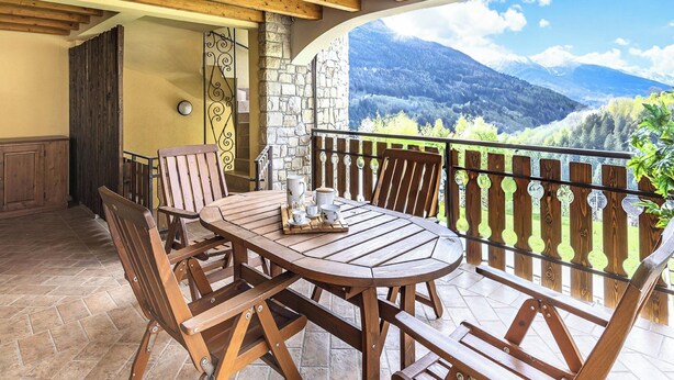 A wooden table and chairs on a balcony with a stone wall and a view of mountains. - Eden View in Incudine (Monno)