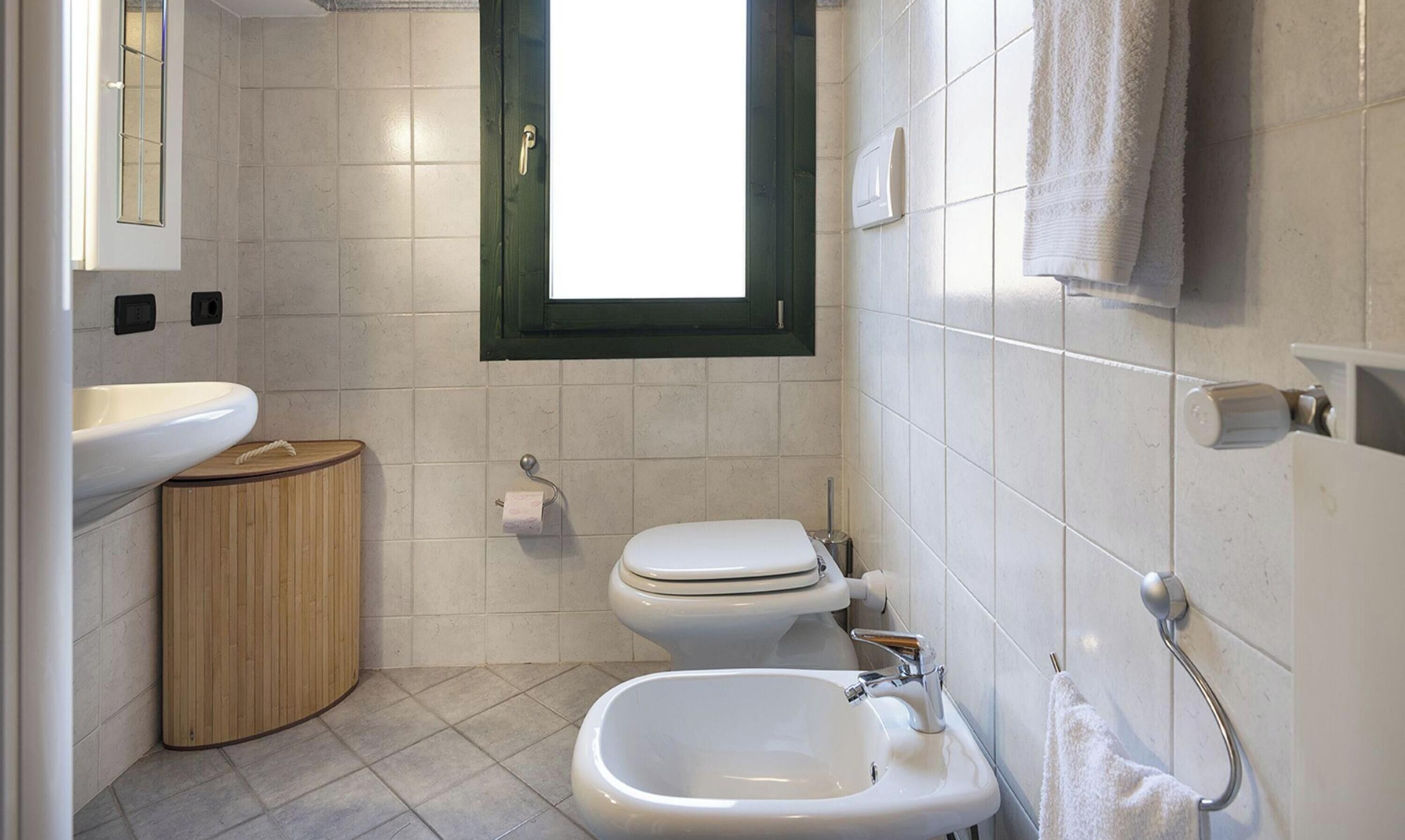 A bathroom with a toilet, bidet, sink, and a window.