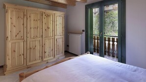 A bedroom with a large wooden wardrobe, a bed, and a balcony with a view of greenery. - Eden View in Incudine (Monno)