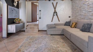 A living room with a sofa, a rug, a wall-mounted ski rack, and a staircase leading to another room. - Eden View in Incudine (Monno)