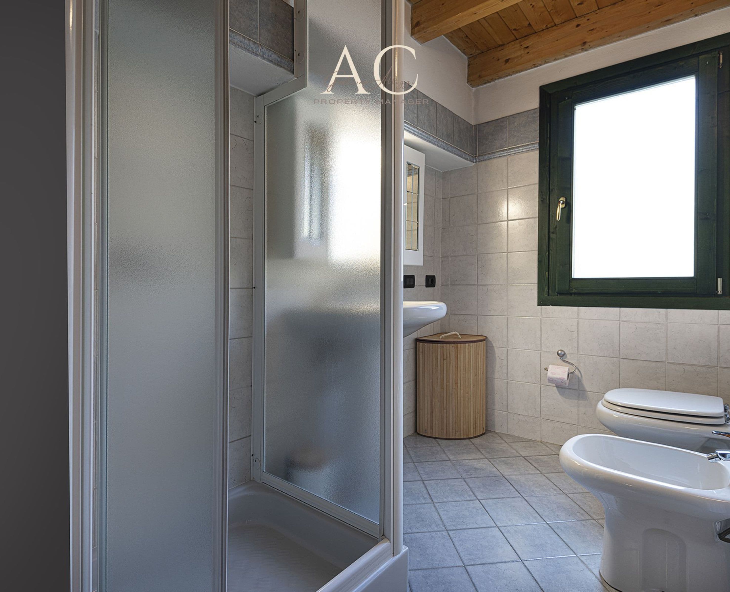 A bathroom with a shower, toilet, and sink, featuring a frosted glass door and tiled walls.
