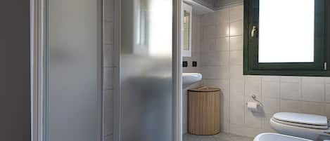 A bathroom with a shower, toilet, and sink, featuring a frosted glass door and tiled walls.