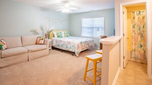 A bedroom with a bed, a sofa, a small table, and a ceiling fan. - Marsh Girl Suite: St. James Studio - Beach Club, Pool & Marina (Southport)