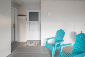 Eine Veranda mit zwei türkisfarbenen Adirondack-Stühlen, einer weißen Tür und einem Willkommen-Schild.
