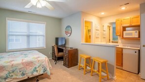 A bedroom with a bed, a desk, and a kitchenette.