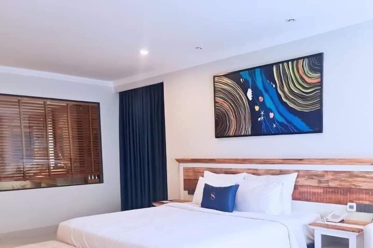 A modern hotel room with a large bed, a bench, a nightstand, and a painting on the wall.
