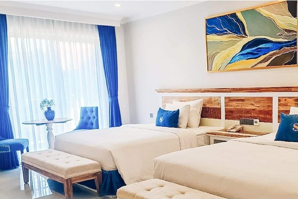 Ein Hotelzimmer mit zwei Betten, einer Sitzecke mit einem Sessel und einem Tisch sowie einem Bild an der Wand.