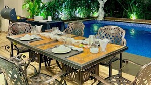 A dining area with a pool view, featuring a table set for four, surrounded by chairs, and a grill in the background. - Sabina Luxury Boutique Hotel & Villa (Ho Chi Minh City)