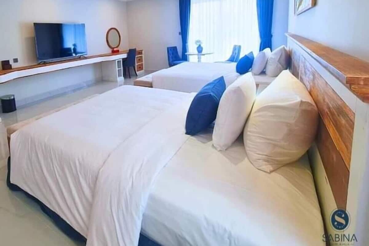 Ein Hotelzimmer mit zwei Betten, einem Fernseher, einem Schreibtisch und einem fenster mit Vorhängen.