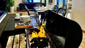 A modern indoor dining area with a grill, tables, chairs, and a TV screen displaying a music video. - Sabina Luxury Boutique Hotel & Villa (Ho Chi Minh City)