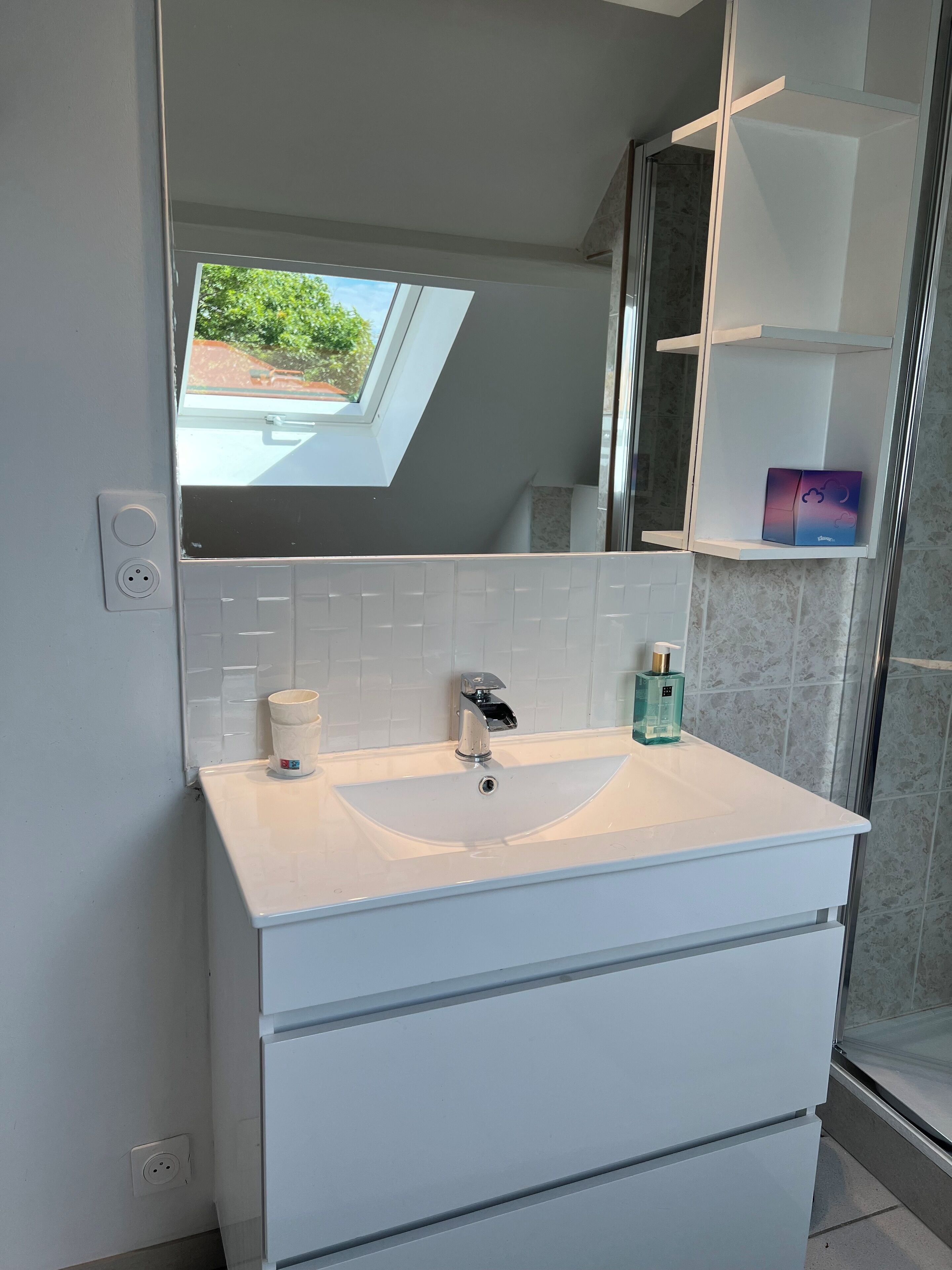 Een moderne badkamer met dakraam, een witte wastafel en een douchecabine van glas.