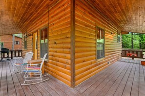 A log cabin with a porch, rocking chairs, and a bench. - Lost In The West Cabin | Hochatown Cabin with Fishing Pond, Hot Tub, Fireplace & Pets (Hochatown)