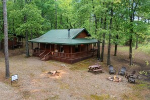 A cabin with a porch, a fire pit, and outdoor seating. - Lost In The West Cabin | Hochatown Cabin with Fishing Pond, Hot Tub, Fireplace & Pets (Hochatown)