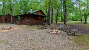 A cabin with a porch, a fire pit, and Adirondack chairs. - Lost In The West Cabin | Hochatown Cabin with Fishing Pond, Hot Tub, Fireplace & Pets (Hochatown)