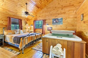 A wooden cabin room with a bed, a hot tub, and a window. - Lost In The West Cabin | Hochatown Cabin with Fishing Pond, Hot Tub, Fireplace & Pets (Hochatown)