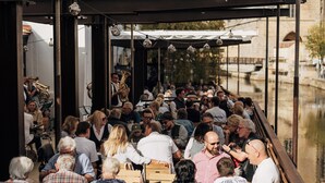 A covered outdoor seating area with tables and benches, overlooking a canal. - Bootshaus Amberg  (Amberg)