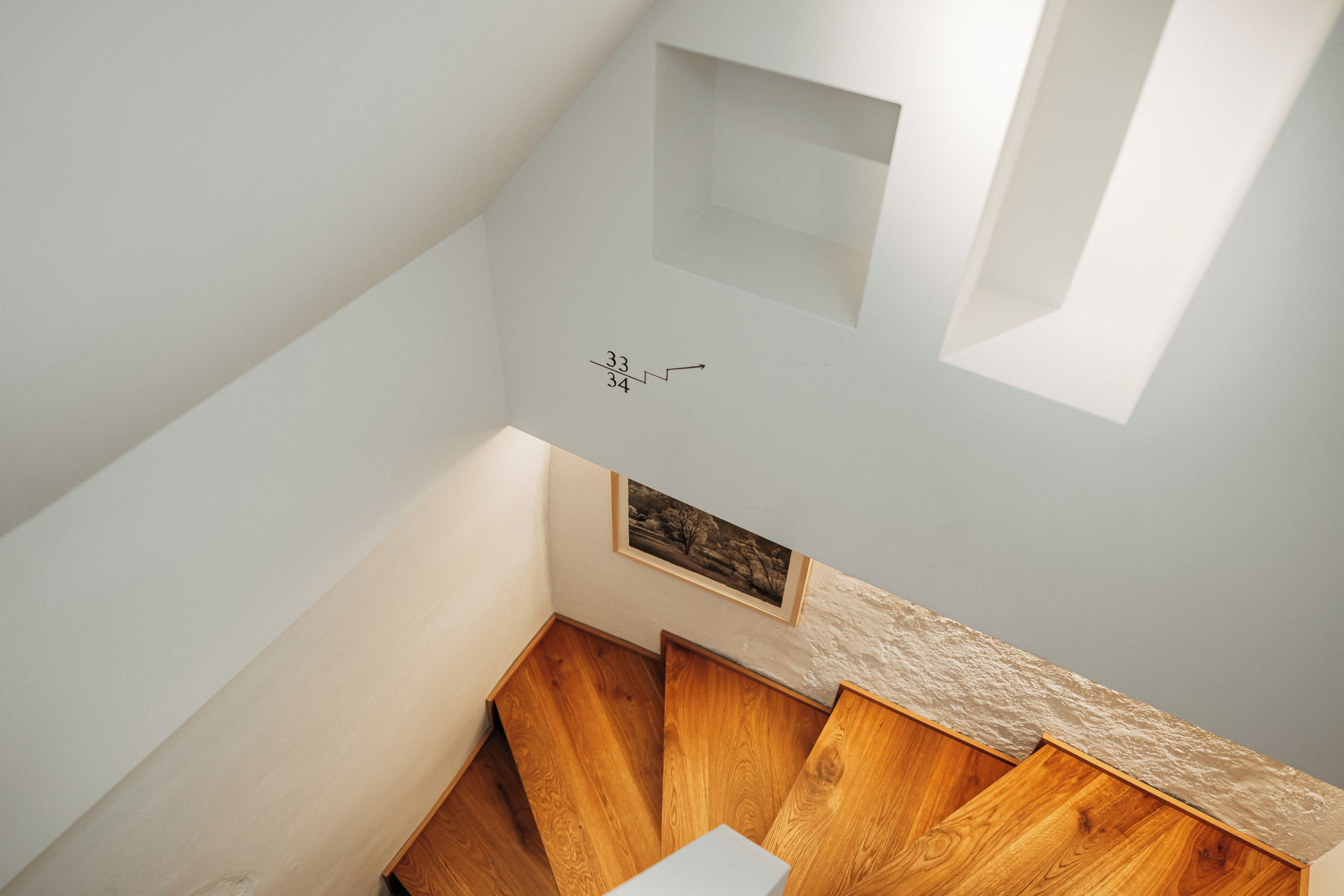 A modern interior with a wooden staircase, a small alcove with a framed picture, and a textured wall detail.