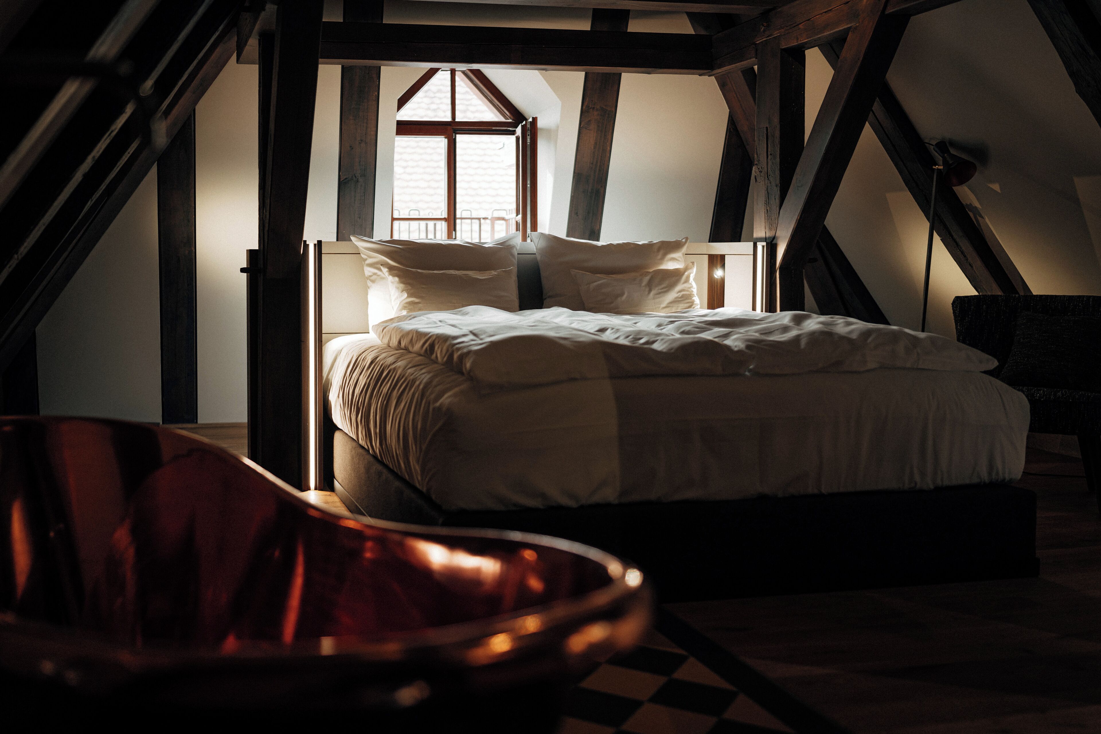Un dormitorio con una cama, una silla y vistas al exterior por una ventana.