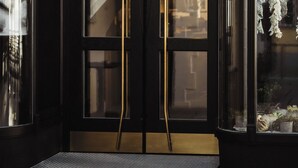 A black double door with a golden handle, a small statue on the roof, and a window with a view of the street. - Bootshaus Amberg  (Amberg)