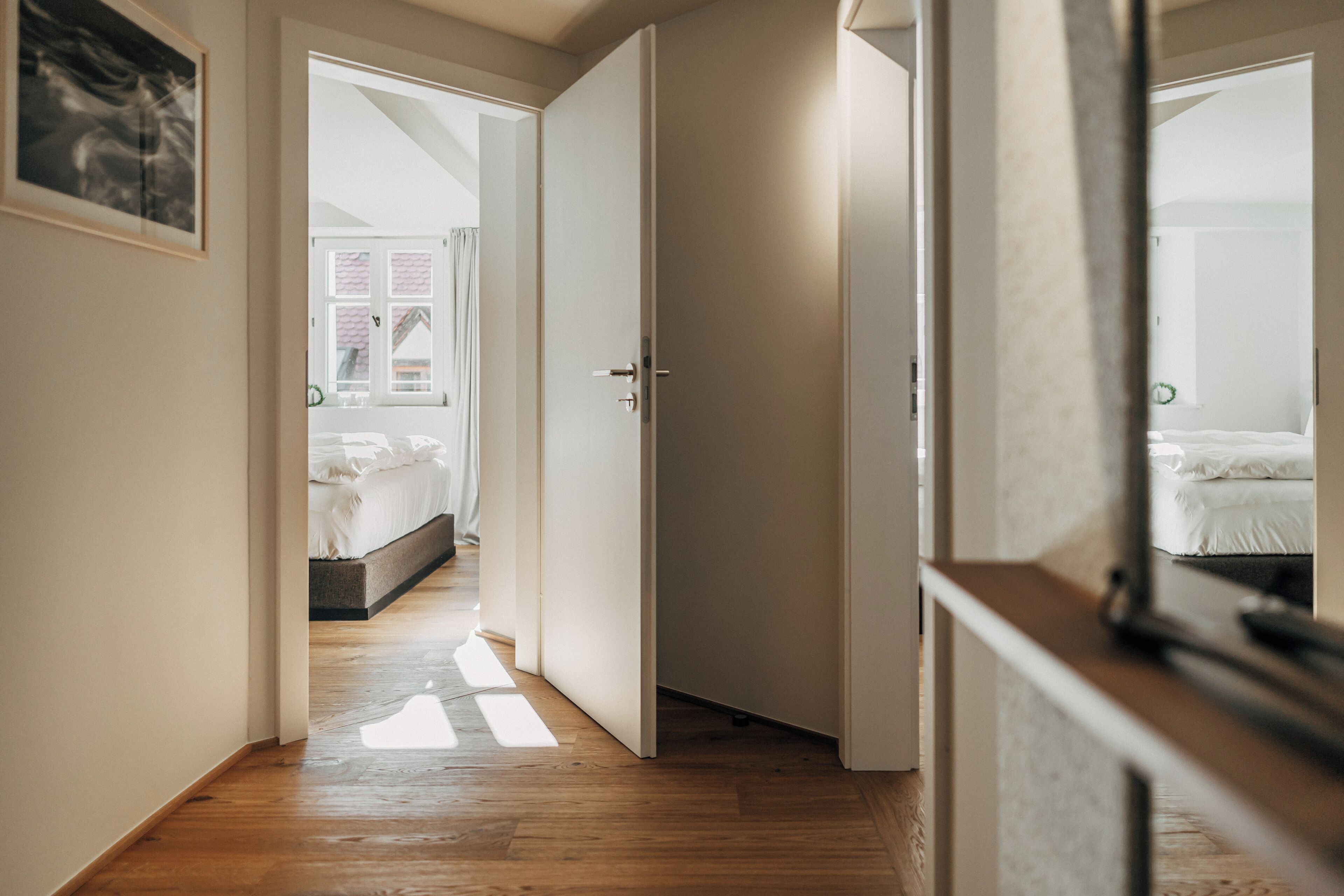 Un estrecho pasillo con suelo de madera que conduce a un dormitorio con cama y ventana.