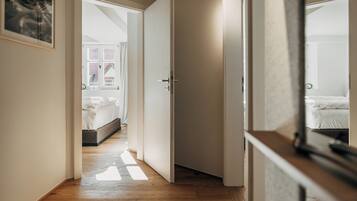 Un estrecho pasillo con suelo de madera que conduce a un dormitorio con cama y ventana.