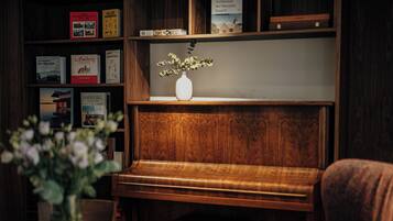 Un pianoforte in legno con un vaso di fiori su una mensola, circondato da librerie piene di libri.
