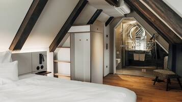 A modern loft bedroom with a sloped ceiling, wooden beams, a bed, a desk, and a chair.