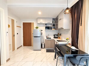 A modern kitchen with a refrigerator, microwave, and stove, a dining table with chairs, and a hanging light fixture. - B305 - 1 Bedroom Serviced Apartment Pool View near Ao Nang Beach (Tambon Ao Nang)